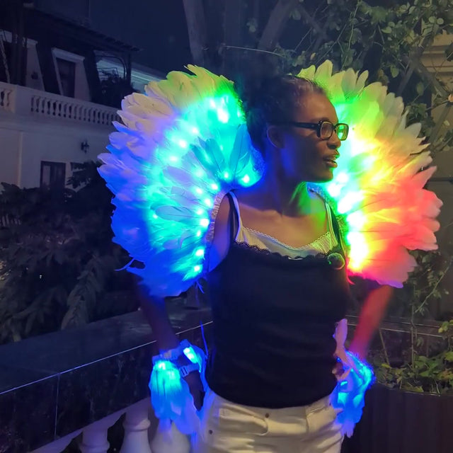 Founder Asia Hall wearing the Aura LED feather back piece with matching LED arm cuffs, the white feathers glowing rainbow, then blue, by remote. Light-up stage wings for showgirls, burlesque, drag and dance performers.