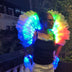 Founder Asia Hall wearing the Aura LED feather back piece with matching LED arm cuffs, the white feathers glowing rainbow, then blue, by remote. Light-up stage wings for showgirls, burlesque, drag and dance performers.