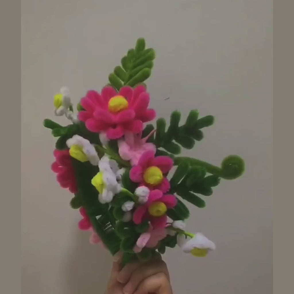 Floral Pipe Cleaner Headband held up and turned to show every side: handmade pink daisies, white blossoms and green fern leaves on a fuzzy green pipe-cleaner band (factory footage)