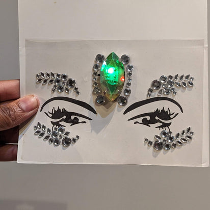 Hand holding rhinestone LED face gem sticker sheet - Adhesive-backed illuminated facial jewelry for easy application before raves, costume parties, Pride celebrations, and beauty photoshoots