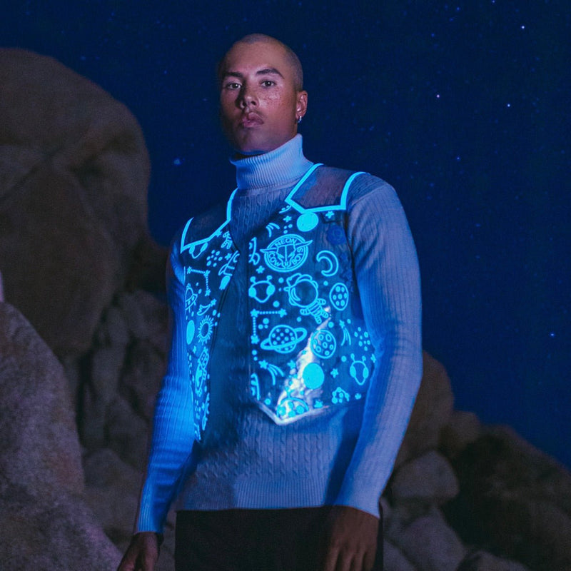 Man under a starry sky in a clear vest glowing blue with space icons over a blue turtleneck, a Neon Cowboys LED space cowboy vest and light up led costume for space cowgirl and cosmic cowgirl looks at festivals, raves and EDM concerts, Neon Cowboys