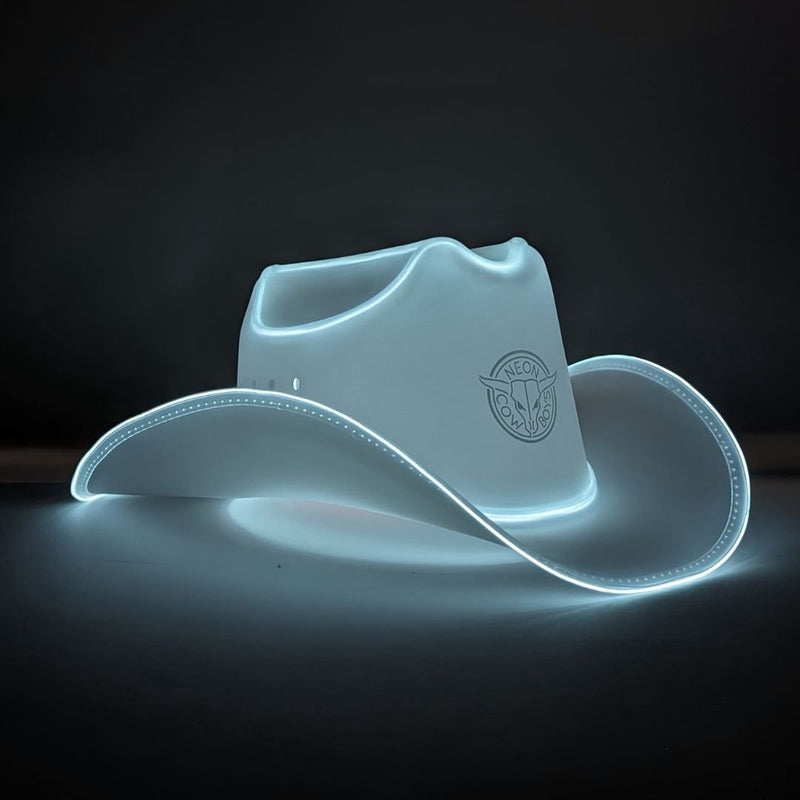 White LED light-up cowboy hat glowing on a dark studio surface, a white light up cowboy hat, neon cowboy hat, LED cowboy hat, great for barn wedding receptions ranch themed celebrations and western bridal parties, loved for weddings, bachelorette parties, nightclub parties, Neon Cowboys